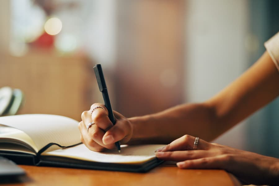 A vingette of a womans hands positioned to write in a notebook.